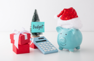 piggy bank wearing santa hate sitting beside tree with note that says budget beside christmas presents